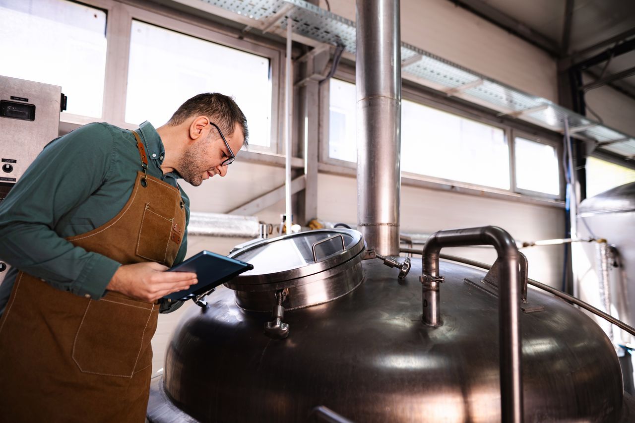 Technicien en microbrasserie vérifiant fermentation sur tablette — méthodologies et indicateurs pour réduire empreinte carbone avec 2050 Analytics